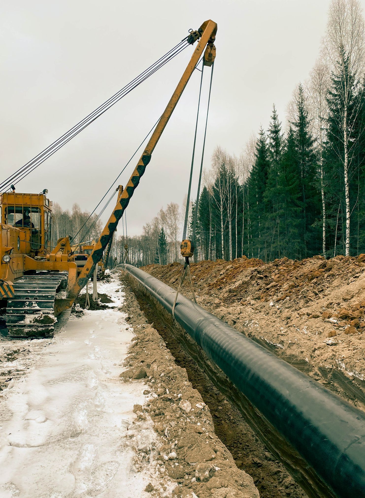 A bulldozer is working on a pipe in the snow.