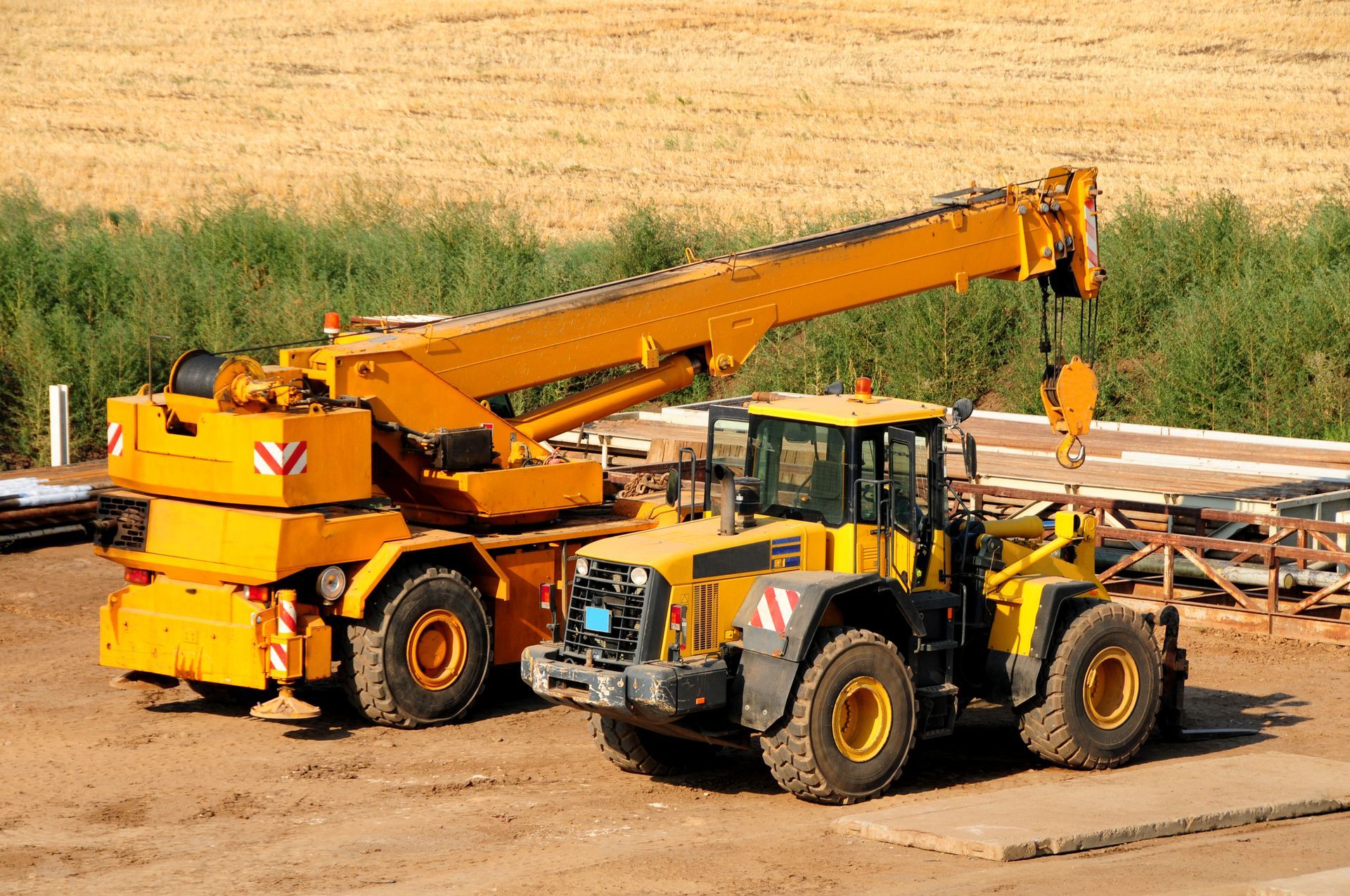 A yellow crane is attached to a yellow tractor on a construction site.