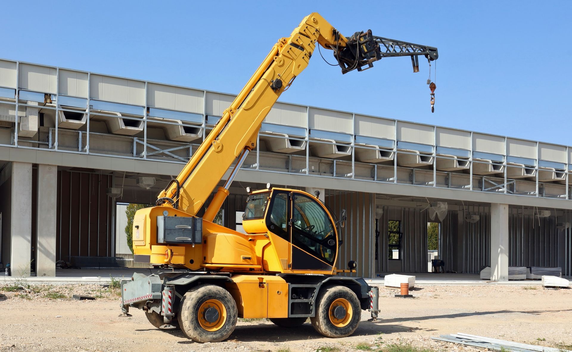 A yellow crane is parked in front of a building under construction.