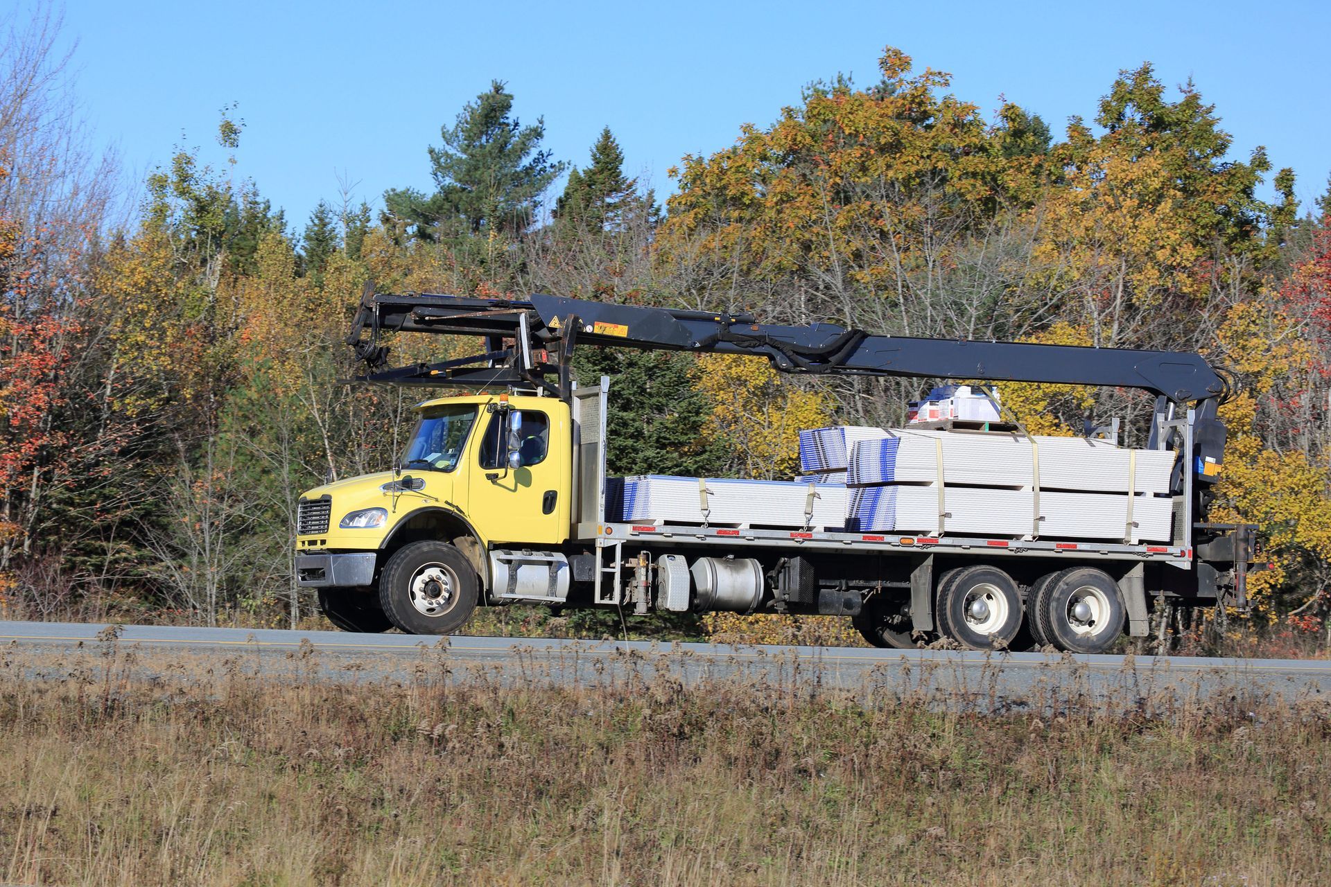 A yellow truck with a crane on the back is driving down a road.