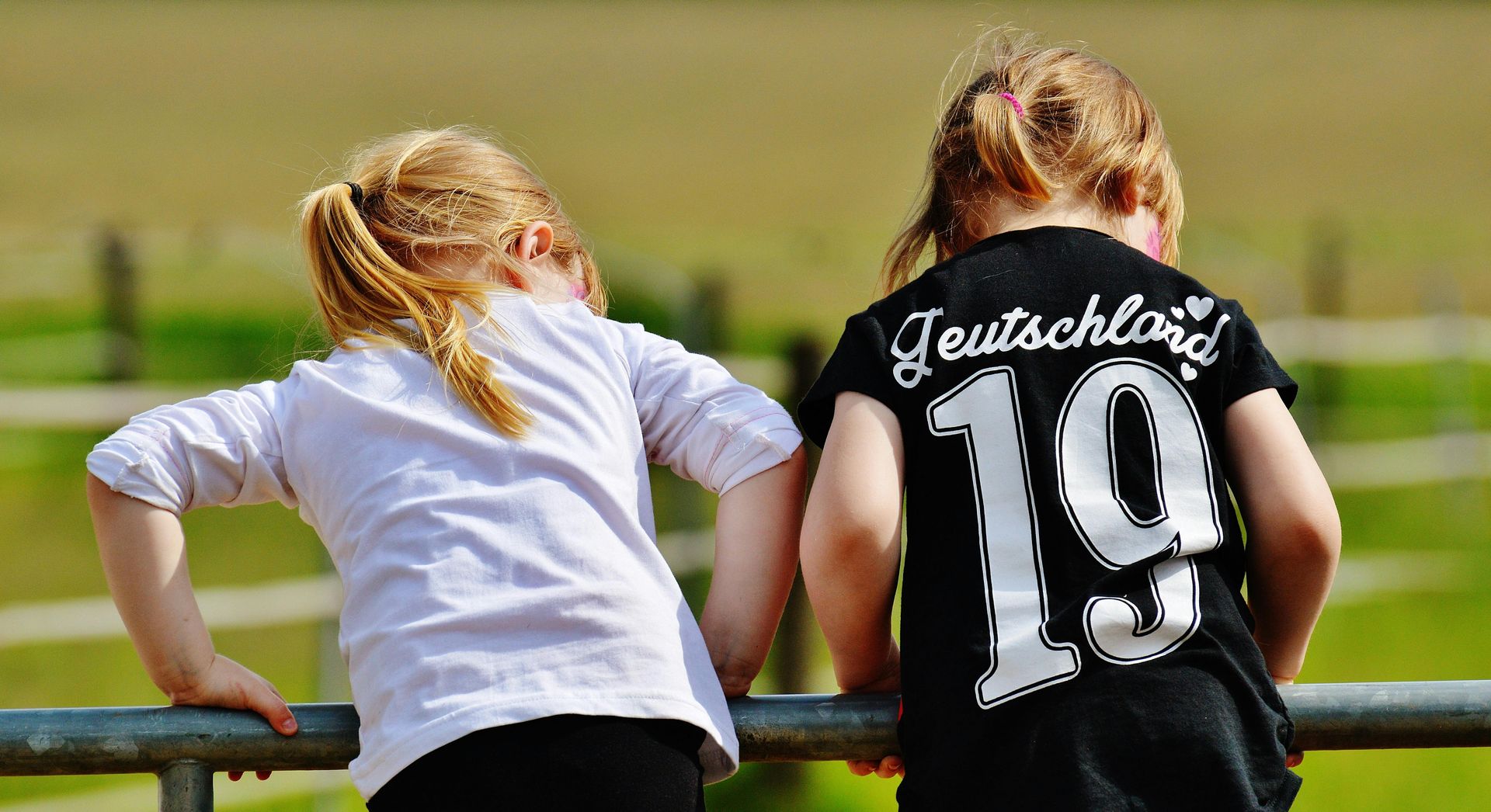 Two little girls are standing next to each other on a railing.