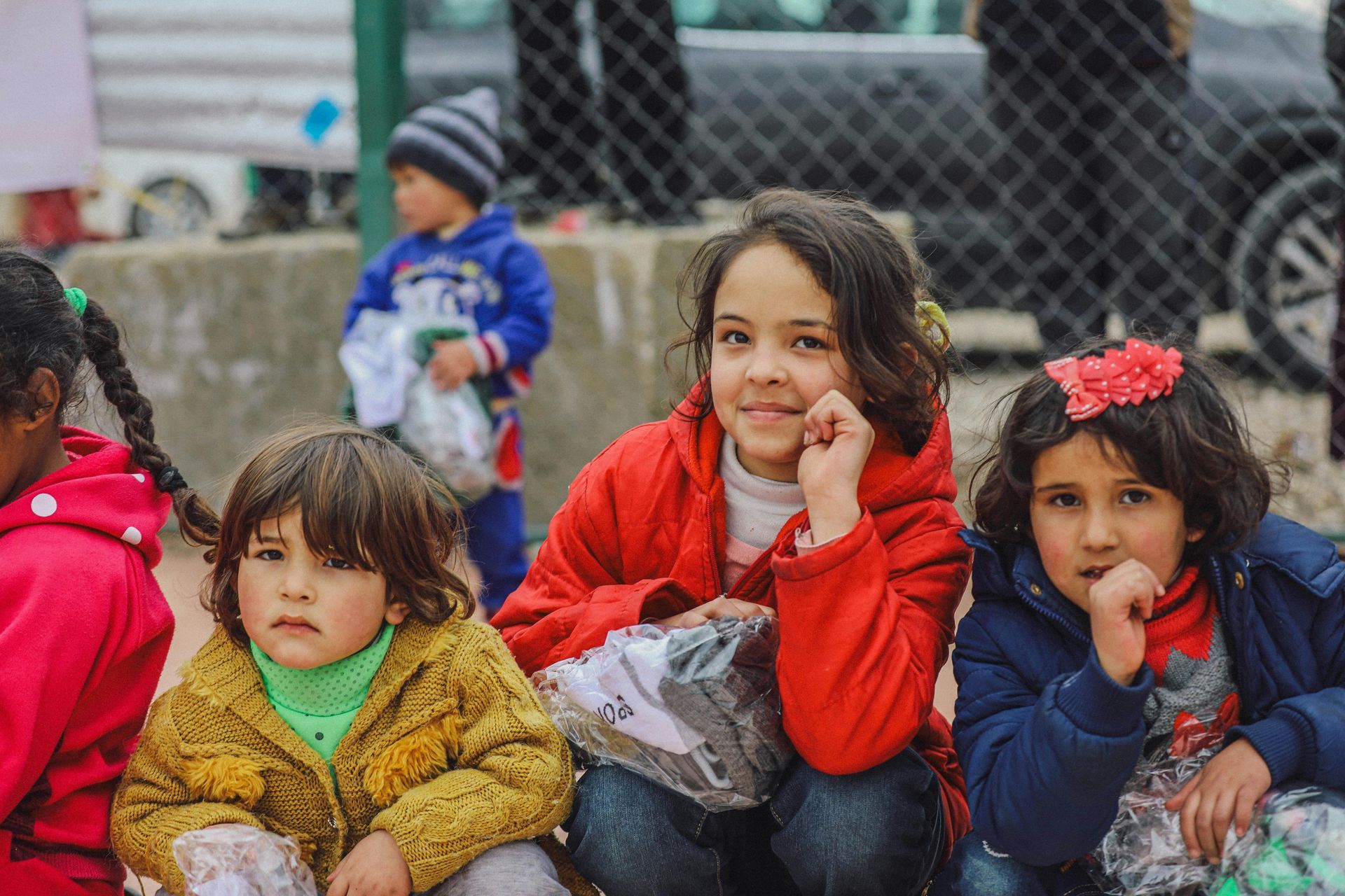 A group of young girls are sitting next to each other in front of a chain link fence.