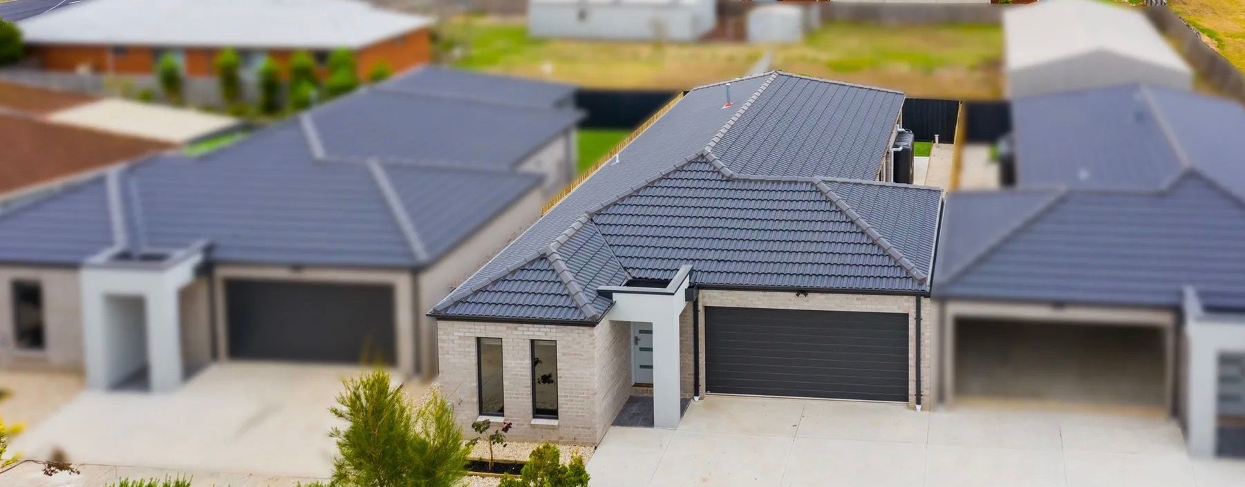Row of modern homes with gray roofs and garage doors, white walls, and a green yard in the distance.