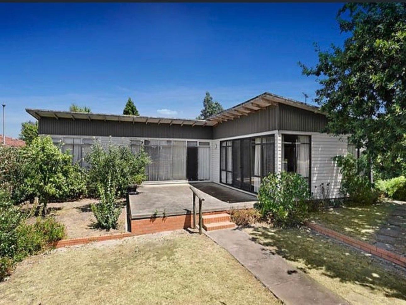 Ranch-style house with flat roof, concrete patio, and small front yard with green lawn.