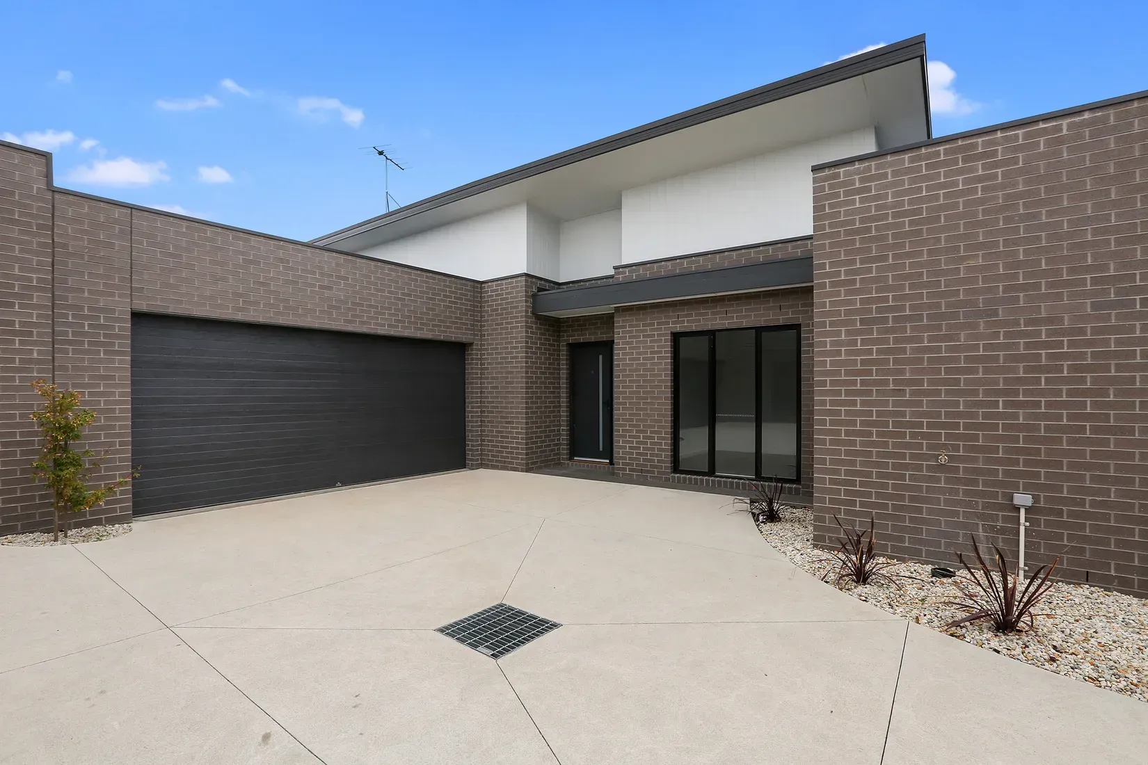 Modern brick townhouse with garage, driveway, and landscaping against a blue sky.