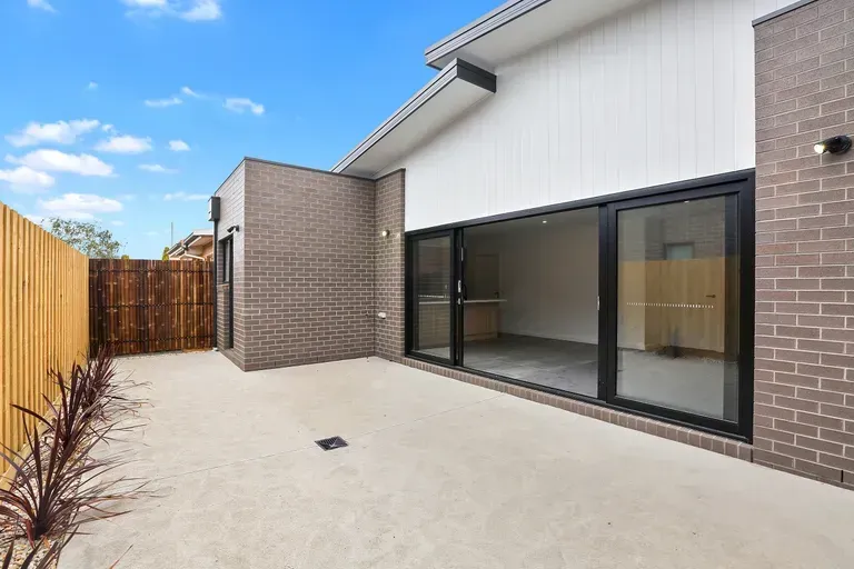 Exterior view of a modern house with a concrete patio, brick walls, and sliding glass doors.