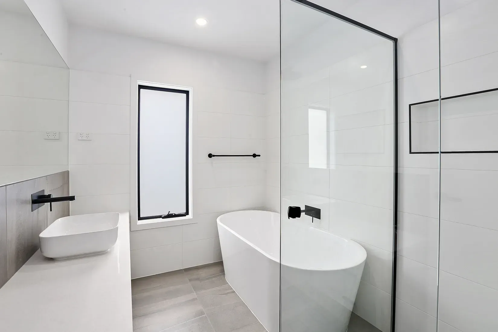 Modern white bathroom with a freestanding tub, glass shower, and rectangular window.