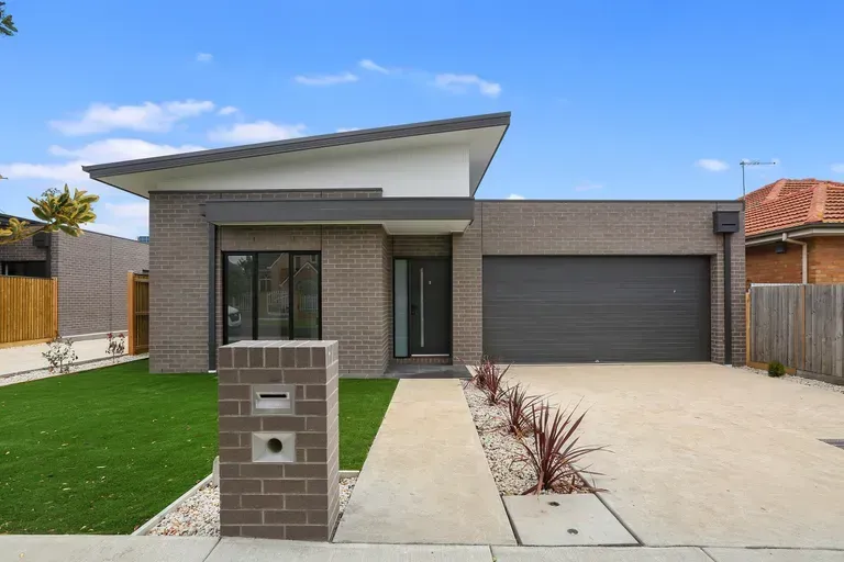Modern brick house with gray roof, garage, and walkway on green lawn.