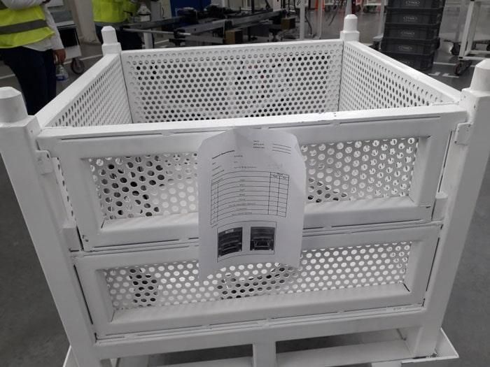 Una cesta blanca con agujeros está en un carro en una fábrica.