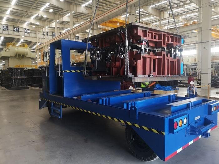 Un camión azul transporta una gran pieza de metal en una fábrica.