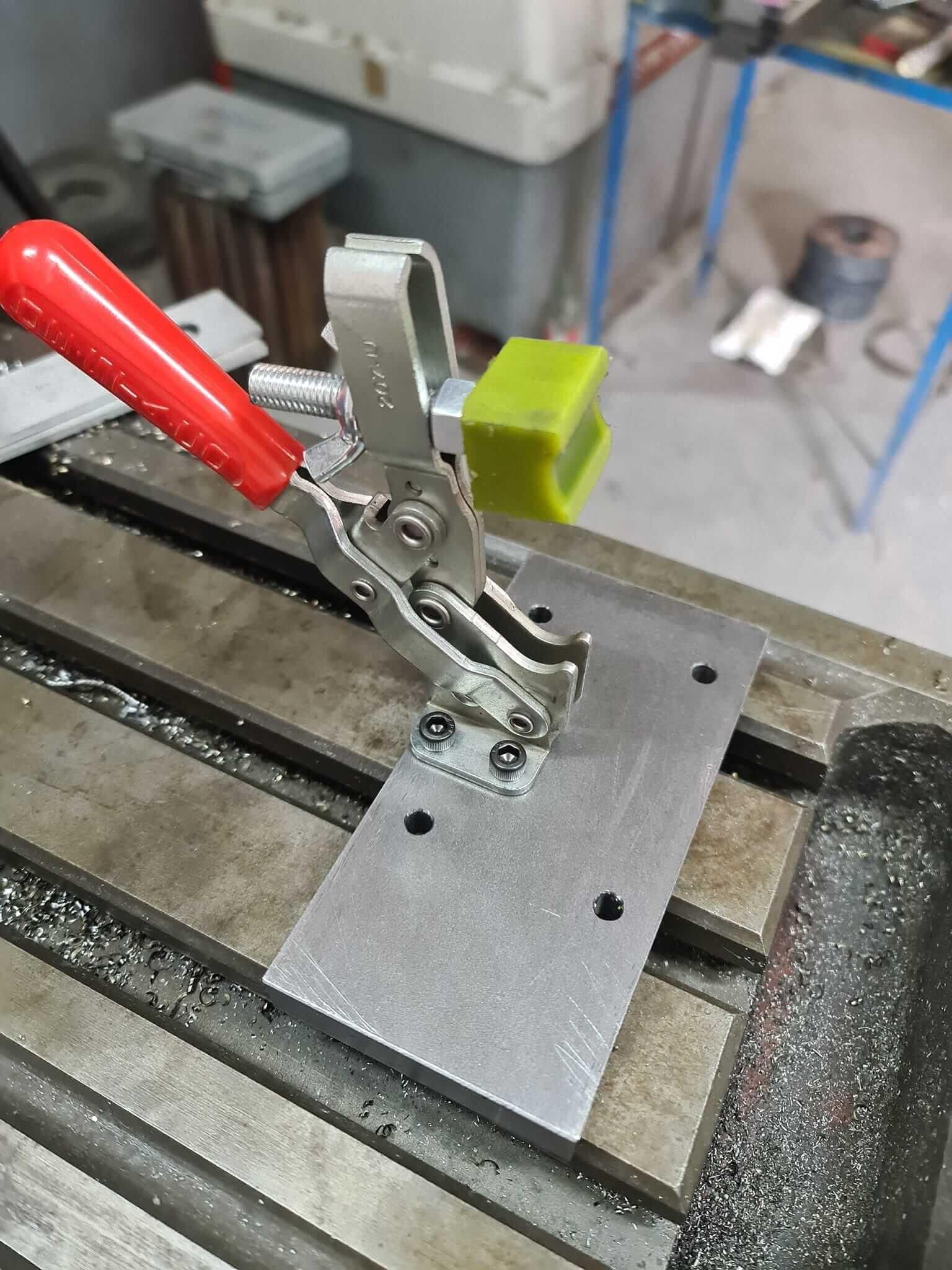 Una abrazadera con un mango rojo está colocada encima de una placa de metal en una máquina.