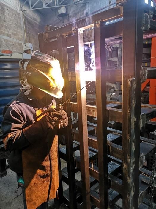 Un hombre está soldando una pieza de metal en una fábrica.