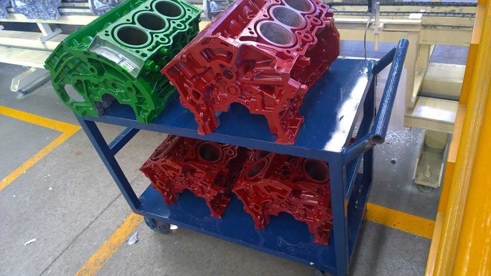 Hay tres bloques de motor sobre un carro en una fábrica.