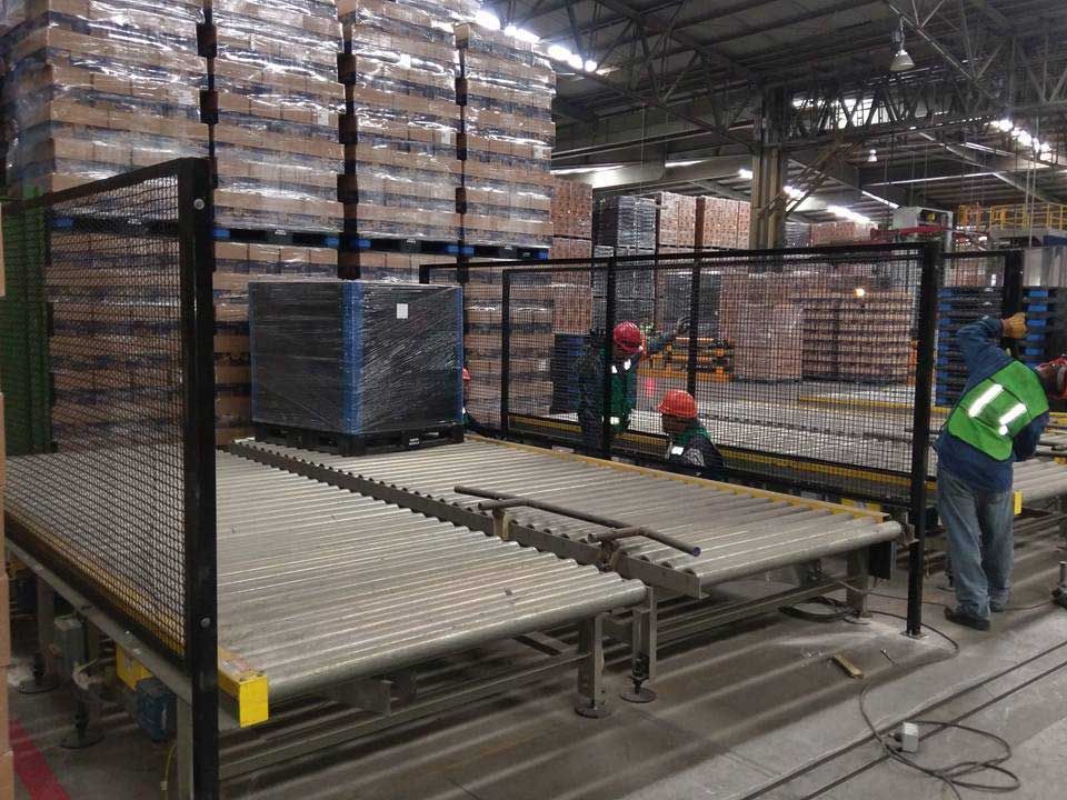 Un hombre con un chaleco verde está trabajando en una cinta transportadora en un almacén.