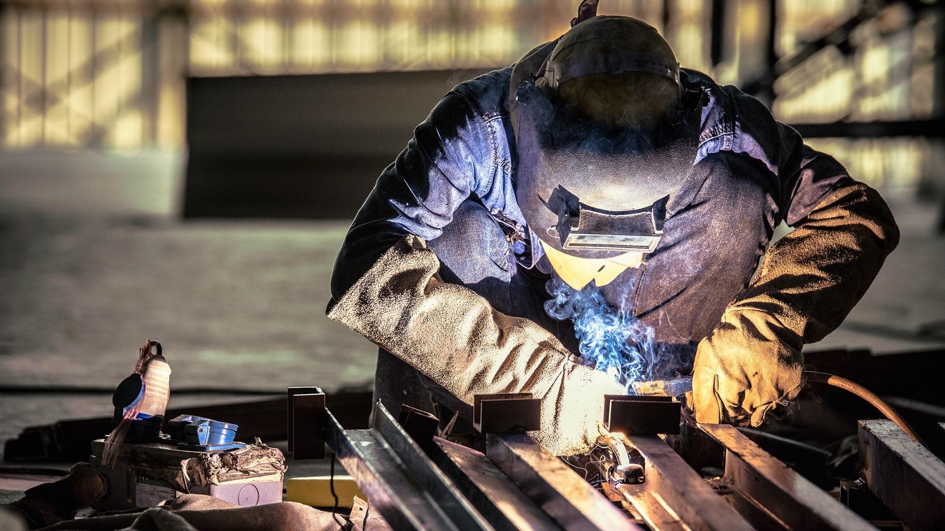 Un hombre está soldando una pieza de metal en una fábrica.