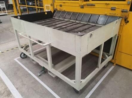 Un gran carro de metal con ruedas se encuentra sobre un piso de concreto en una fábrica.