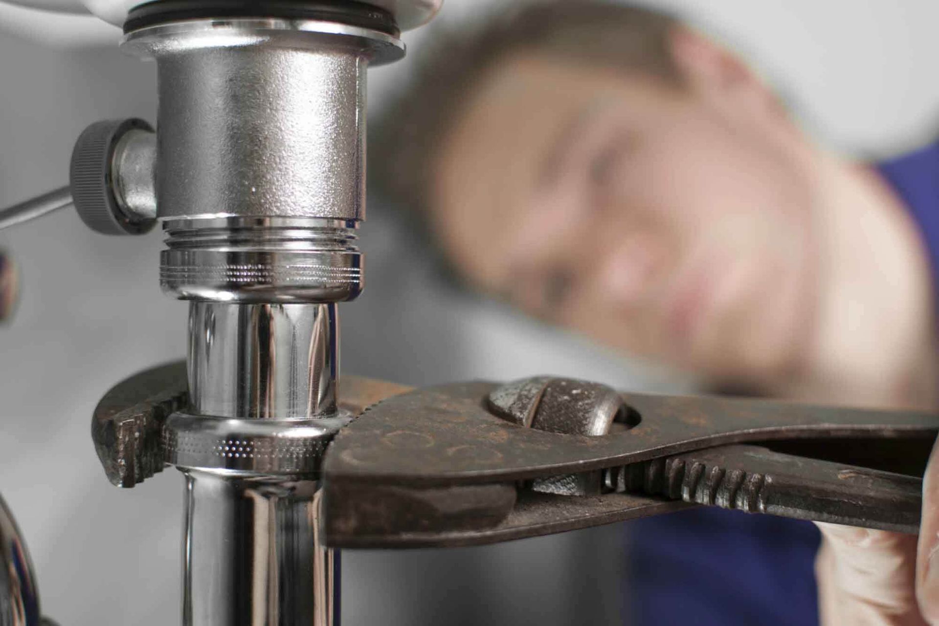 A plumber is fixing a sink with a wrench.