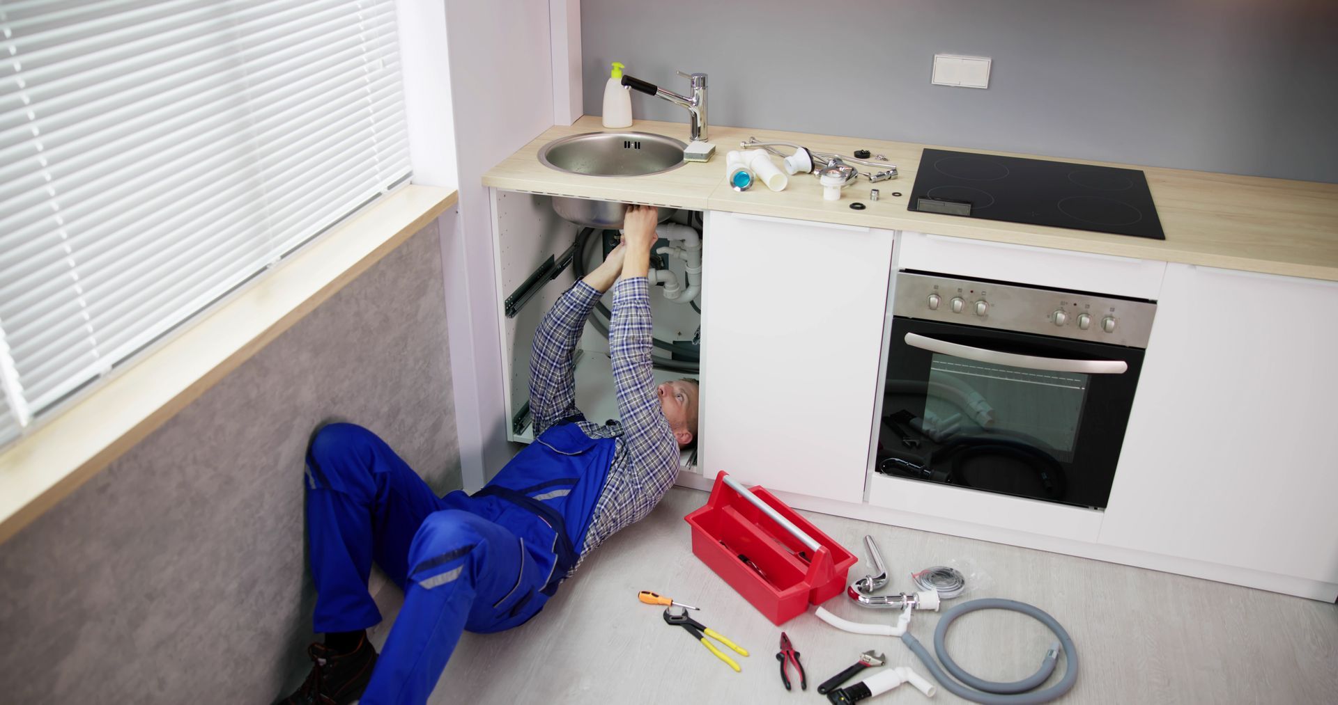 A plumber is laying on the floor fixing a sink in a kitchen.