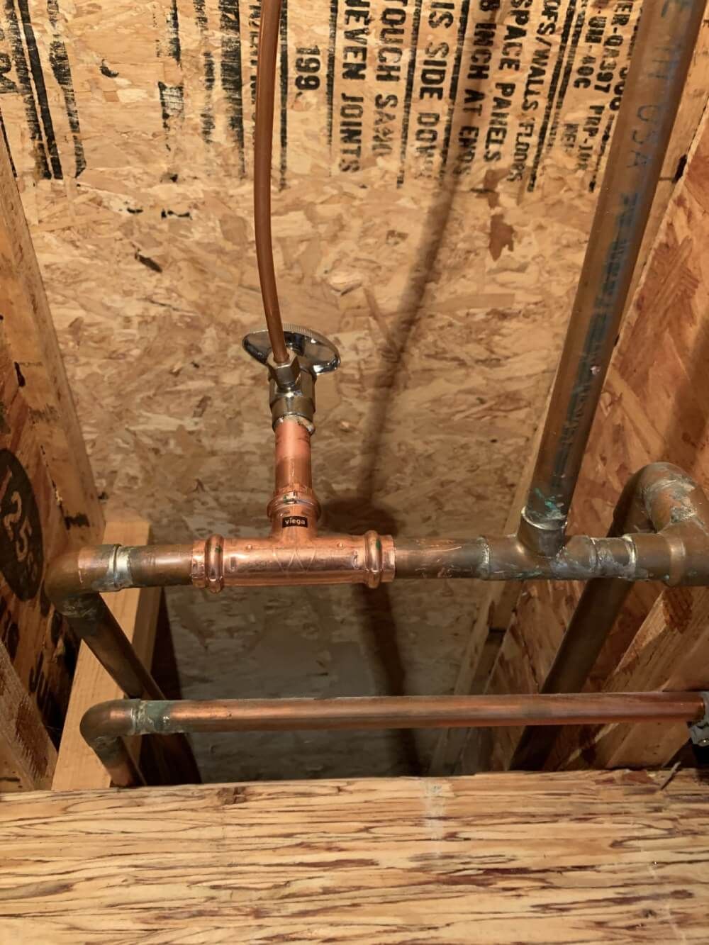 A copper pipe is being installed in a wooden wall.