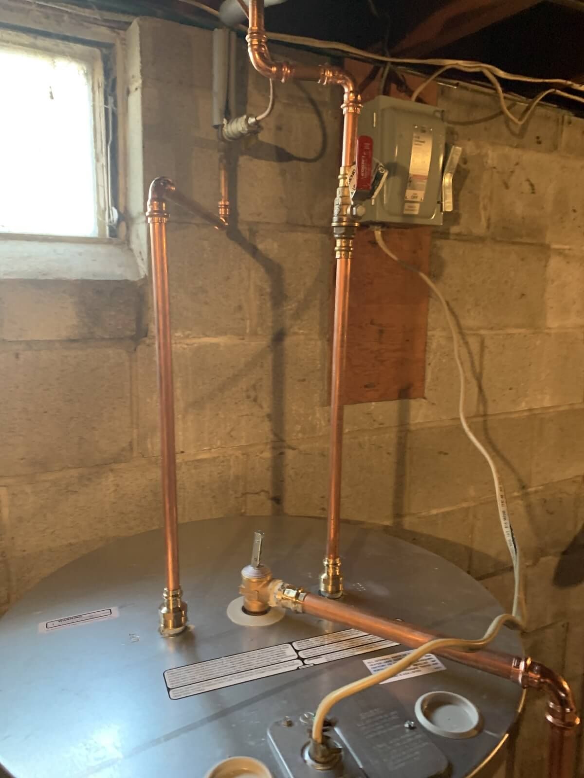 A water heater is sitting in a basement next to a window.