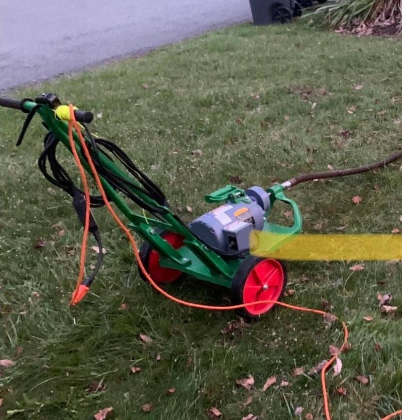 A green lawn mower with a chainsaw attached to it