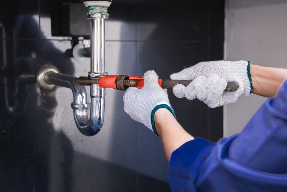 A plumber is fixing a sink pipe with a wrench.