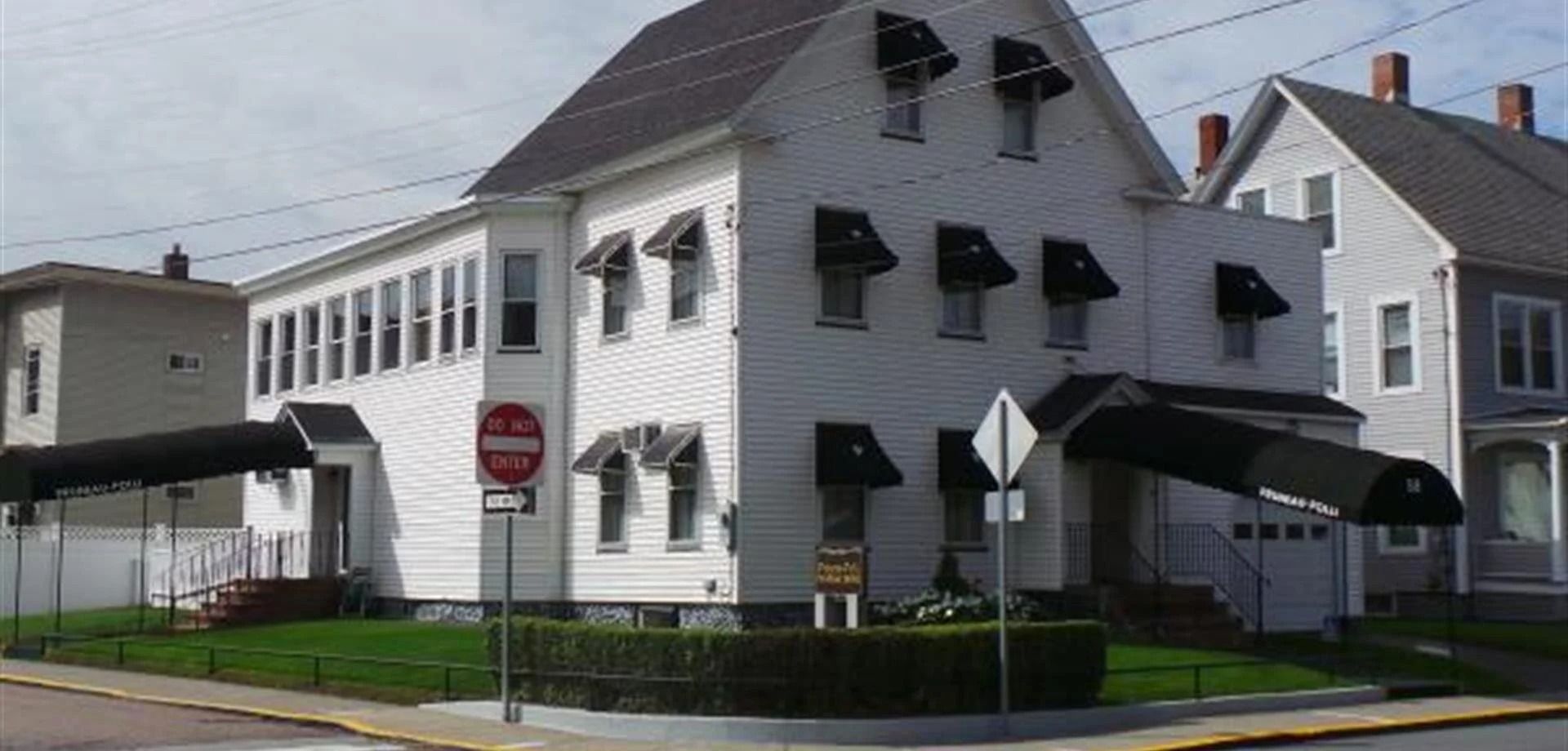 Brick building with storefront and residential floors, sepia tone. A car is parked on the side.