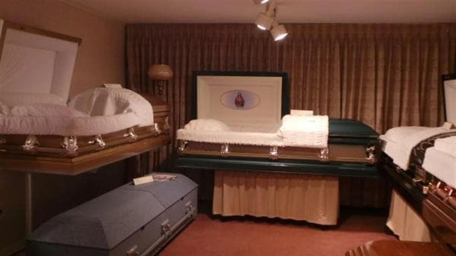 Casket display room with several open coffins, brown curtains, and a pink rug.