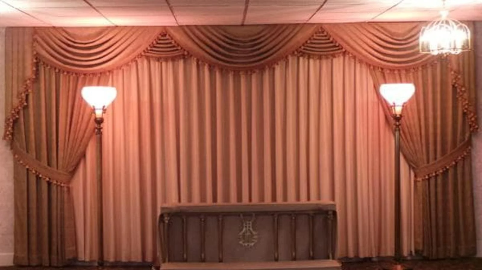 Funeral home with gold drapery, altar, and sconce lighting.