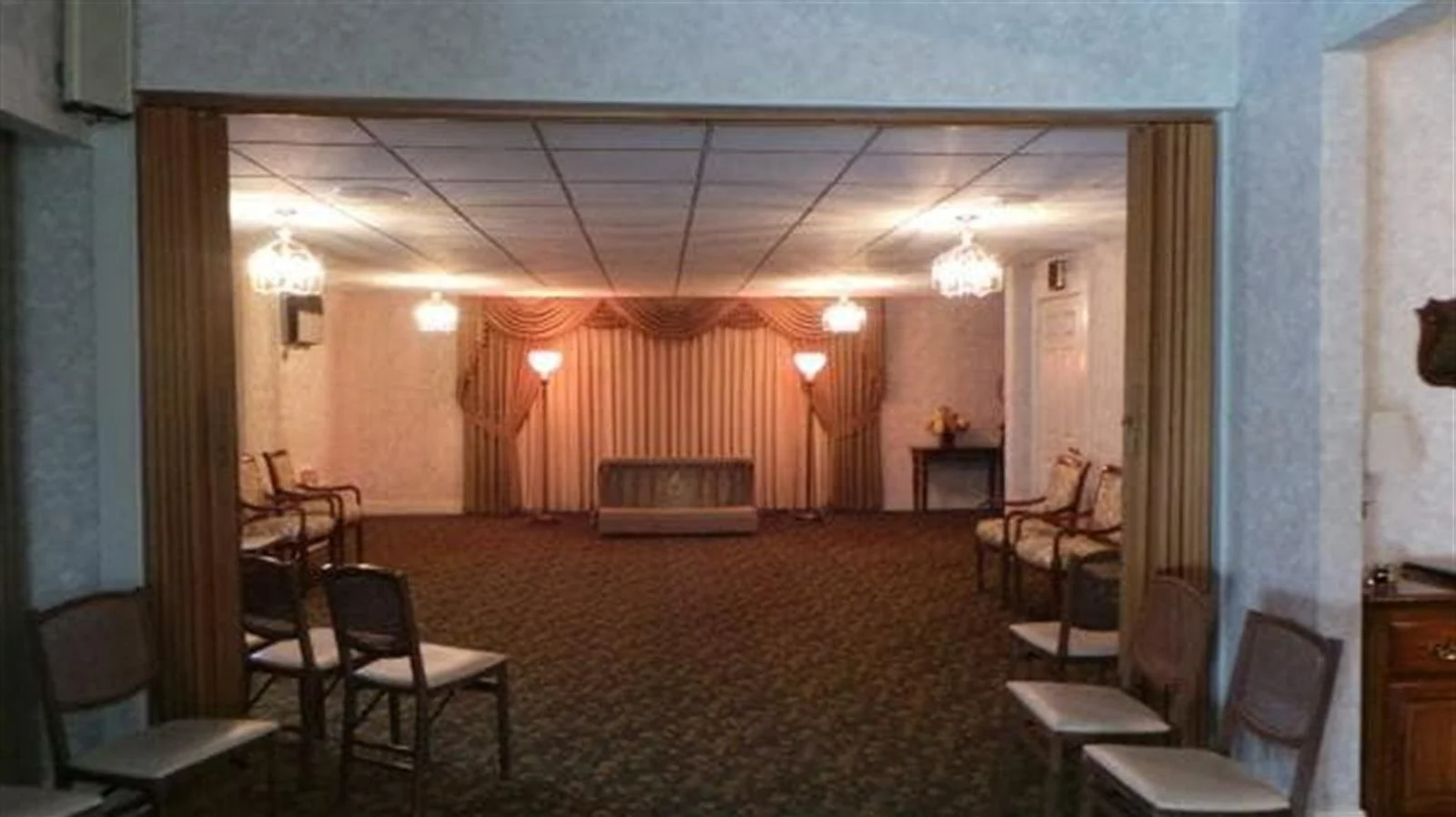 A funeral home chapel with chairs, a raised platform, and draped walls.