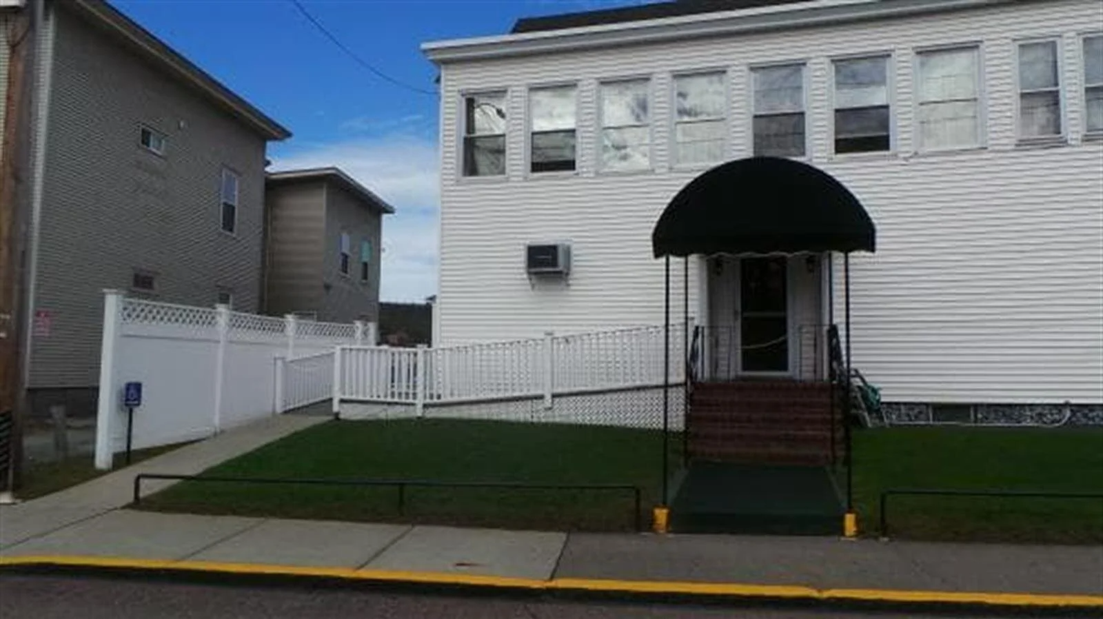 White building with a black awning over the entrance. A ramp and white fence lead to the entrance.