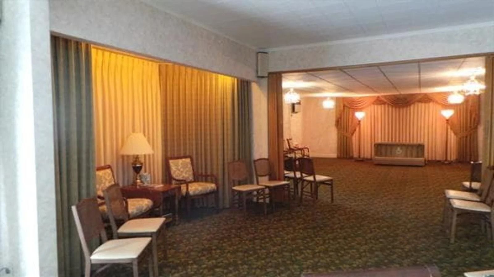 Interior view of a funeral home; chairs arranged near draped curtains and carpeted floors.