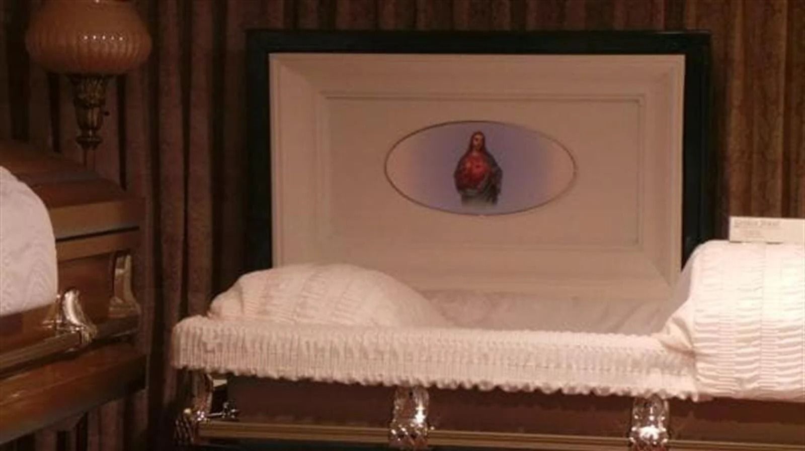 An open white casket with a decorative interior; another closed casket is nearby.