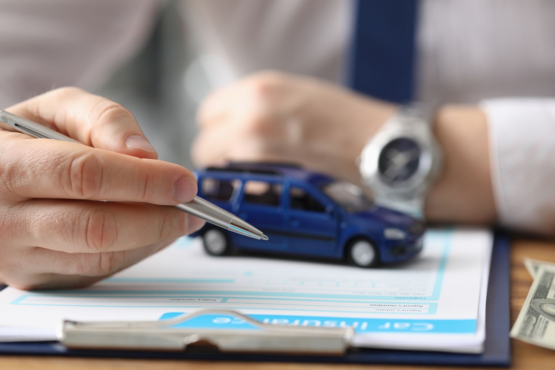Male hands hold a pen over a car insurance form and toy car.