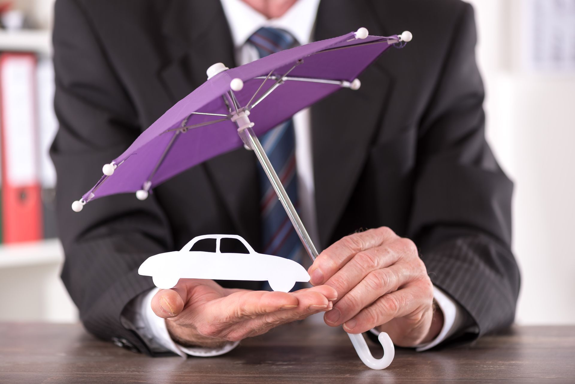 A man is holding a white paper car with a hand and a small purple umbrella with the other.