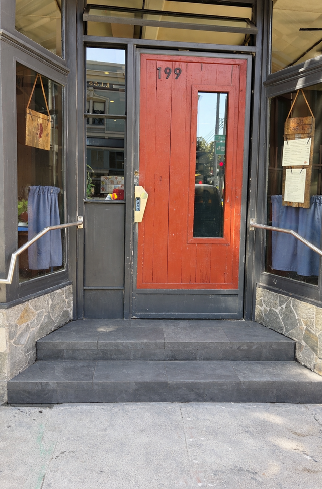 Red front door with a narrow window at a building entrance, framed by stone steps and dark glass sidelights.
