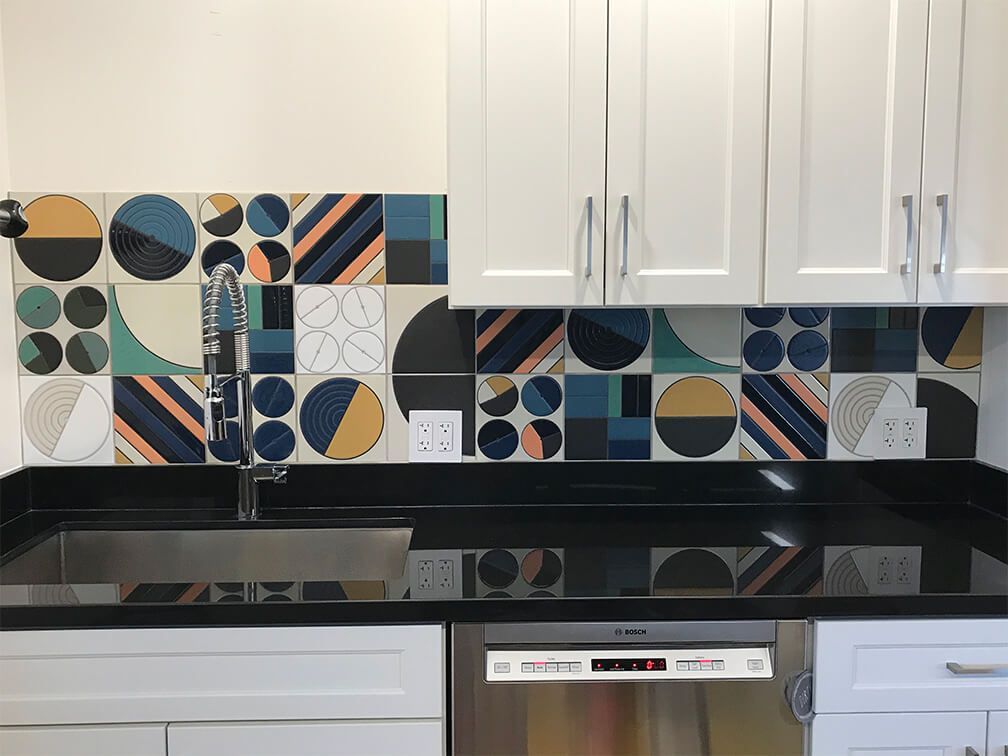 Modern kitchen with white cabinets, black countertop, and colorful geometric tile backsplash