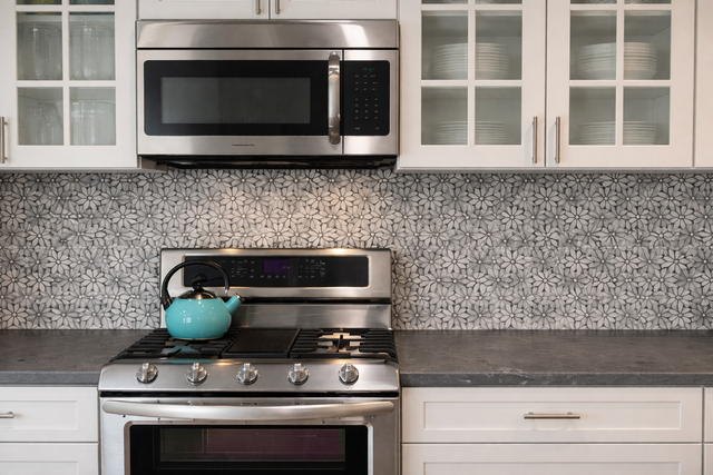 Modern kitchen with stainless steel stove and microwave, white cabinets, and a turquoise pot on the stove
