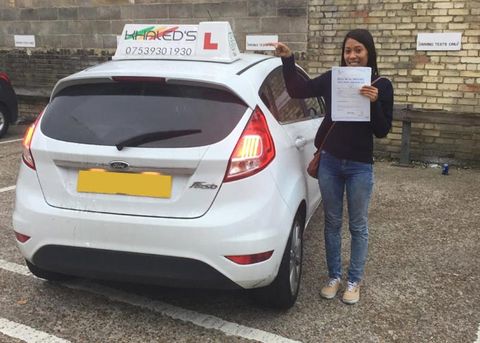 Smiling woman who has passed her driving test stands next to white car
