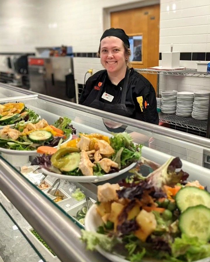 A woman is standing behind a counter filled with plates of food.