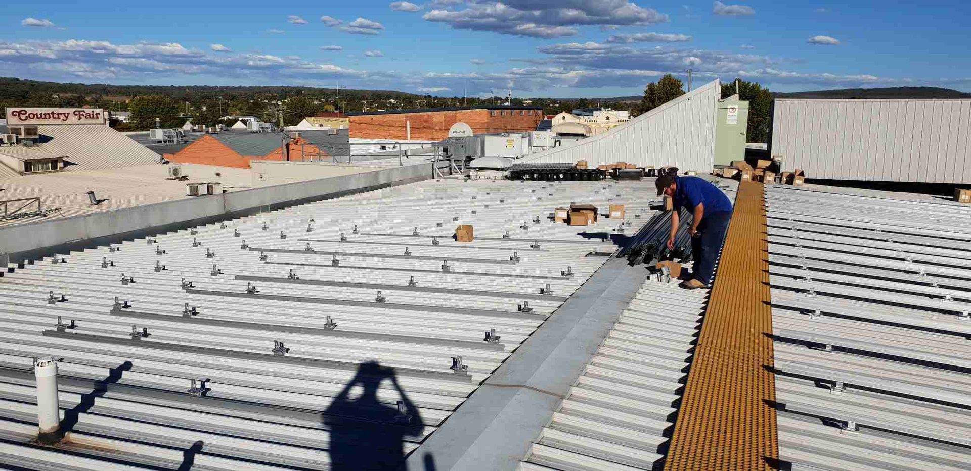 A Man is Working on the Roof of a Building — Sapphire City Solar & Electrical In Glen Innes, NSW