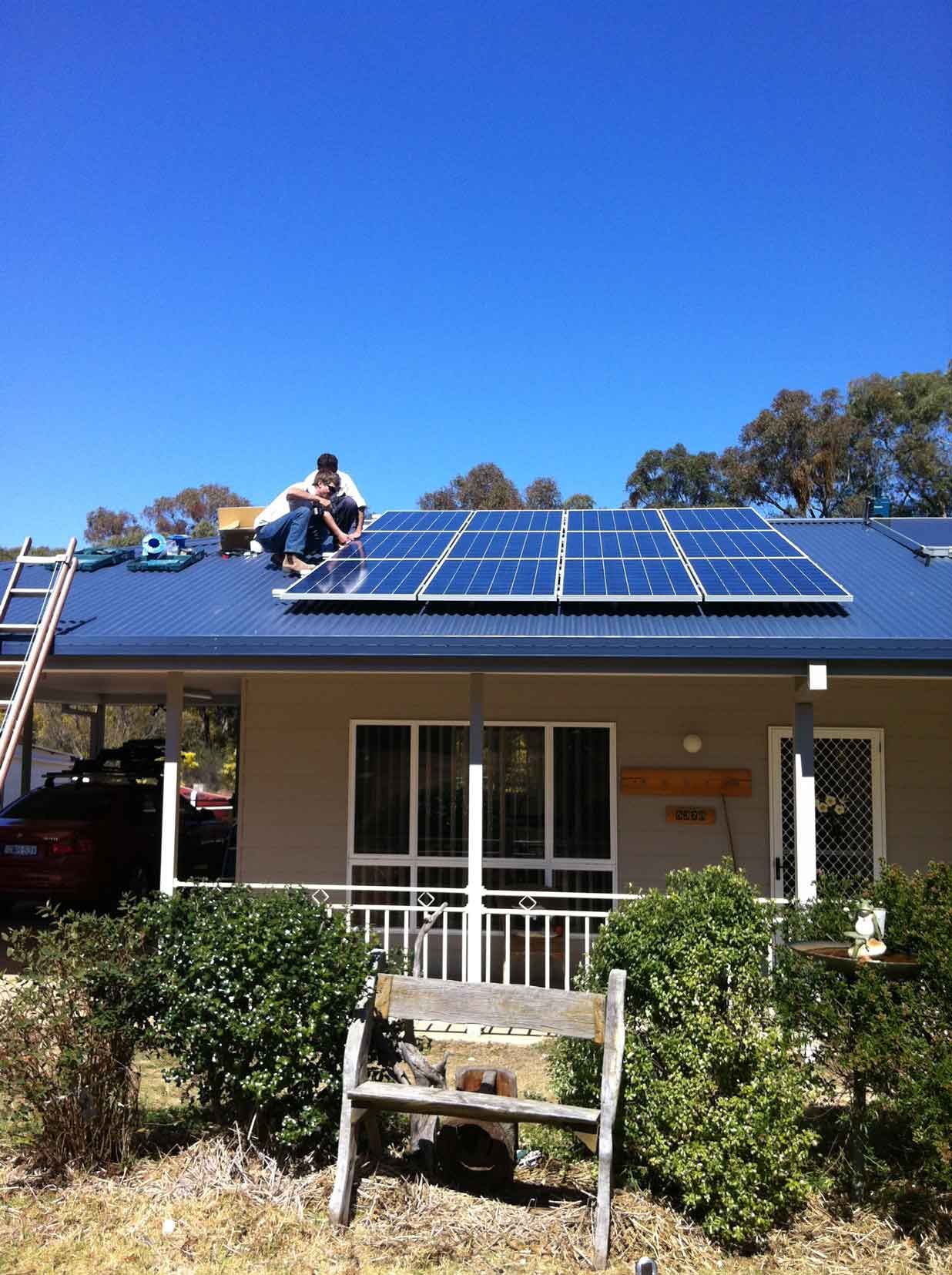 A Man is Sitting on the Roof of a House With Solar Panels on It β Sapphire City Solar & Electrical In Inverell, NSW