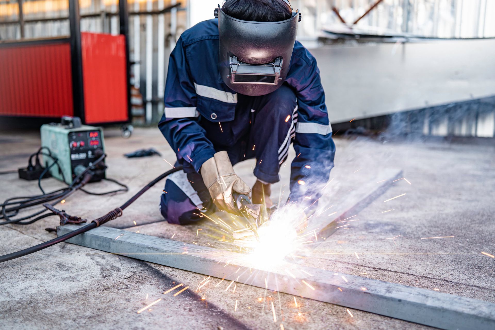 Welder in protective gear welding a metal beam, bright sparks flying in a workshop.