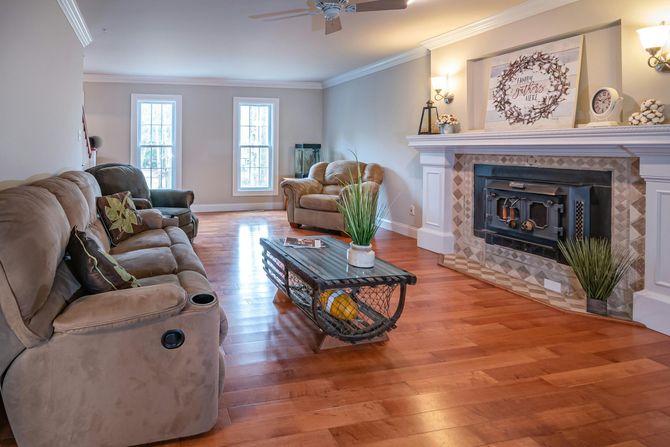 A cozy living room with a tan reclining sofa, two armchairs, a glass coffee table, and a fireplace with a wood stove.