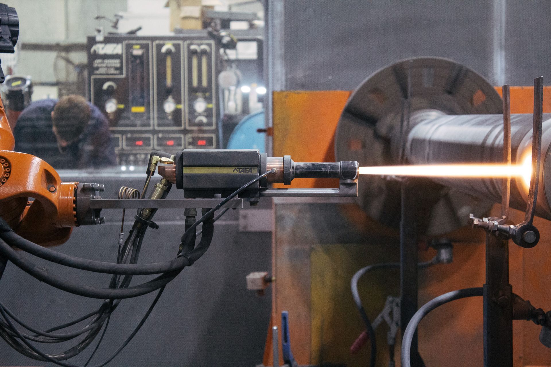 A robotic arm welds a pipe inside a factory, demonstrating cutting-edge technology in thermal spraying services at New Metal Surfaces.