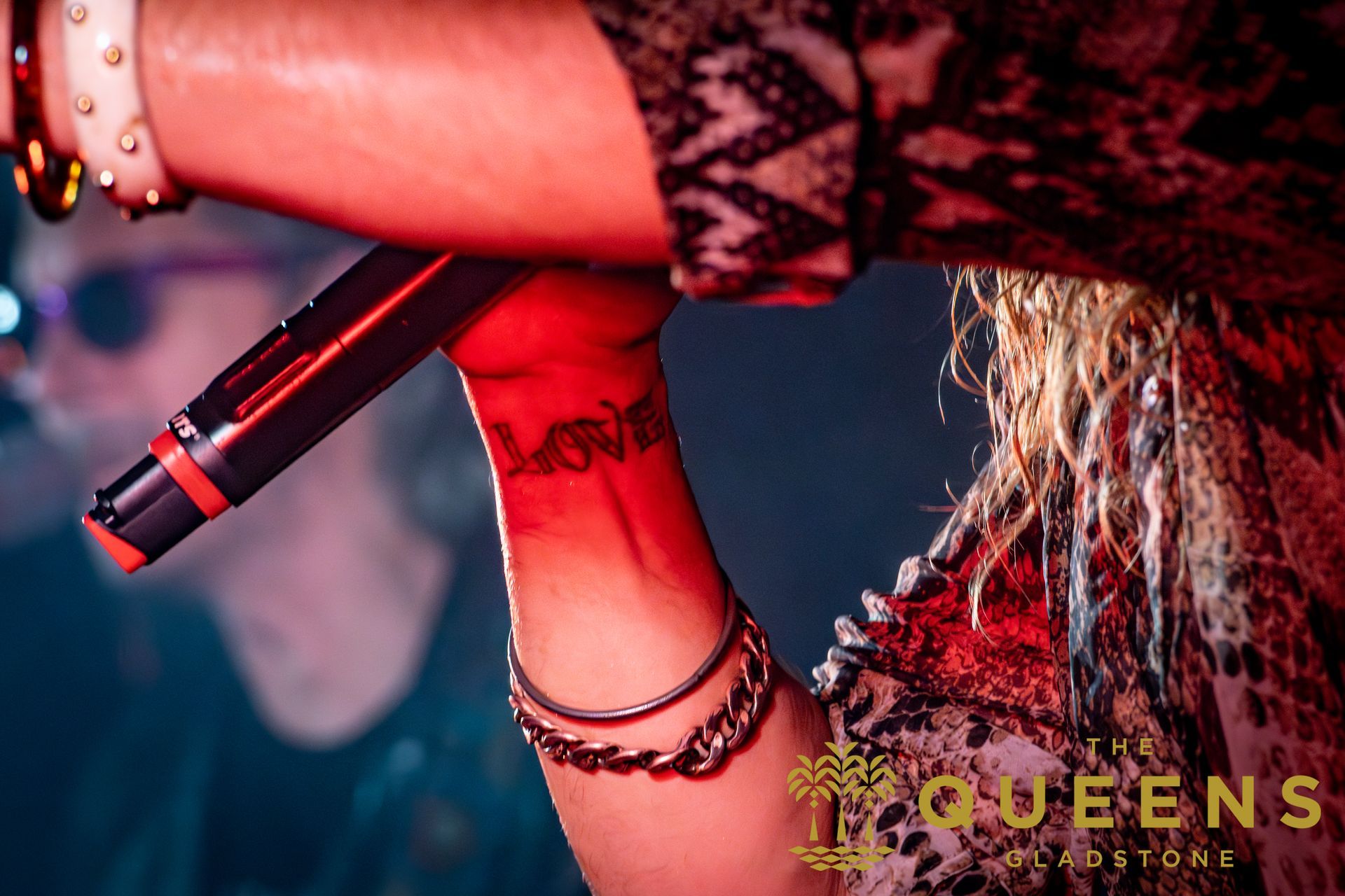 Singer holding a microphone on stage, with red lighting and long hair visible at right