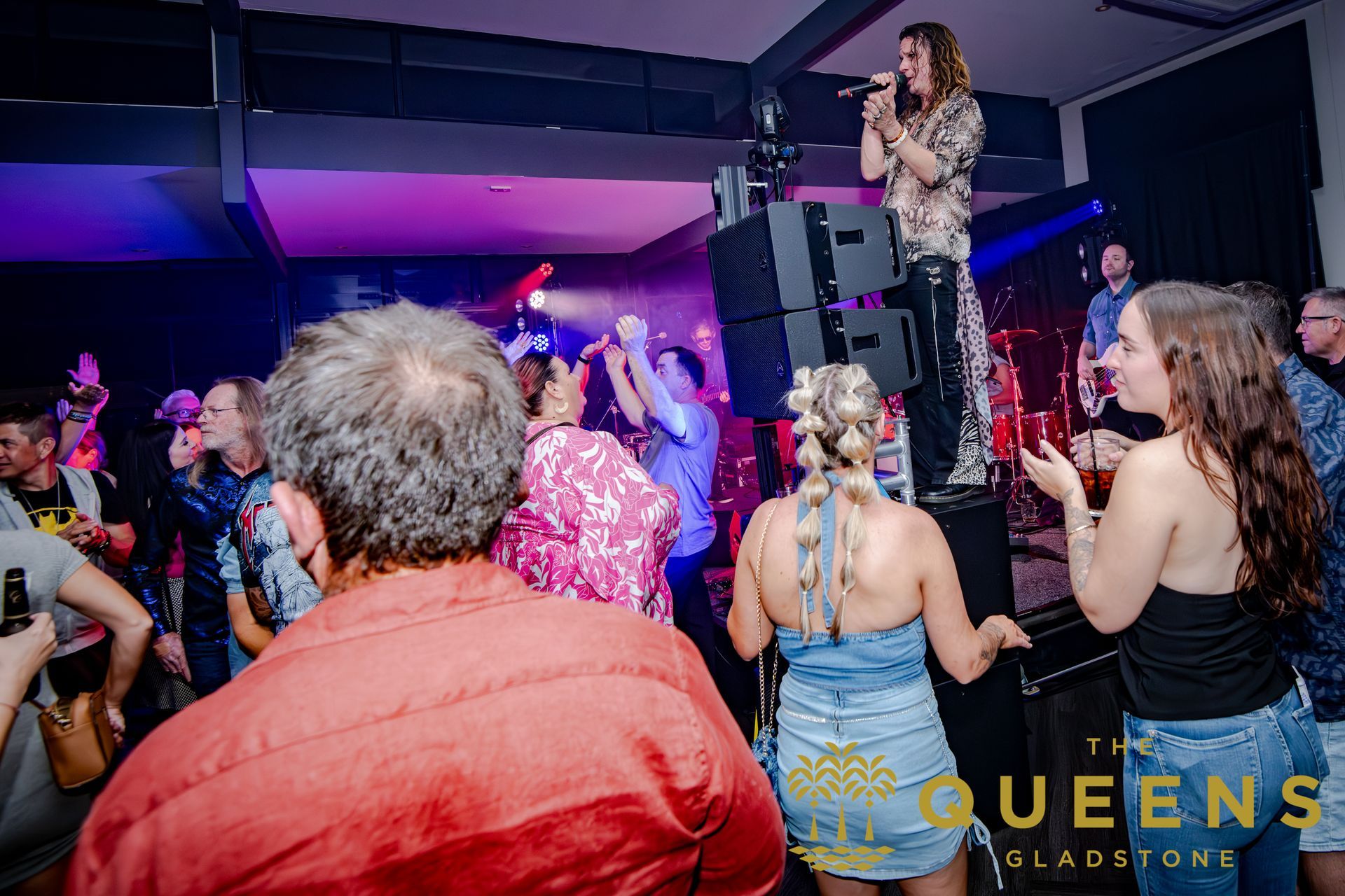 Singer performing on stage at a lively nightclub, with audience dancing and clapping under colorful lights