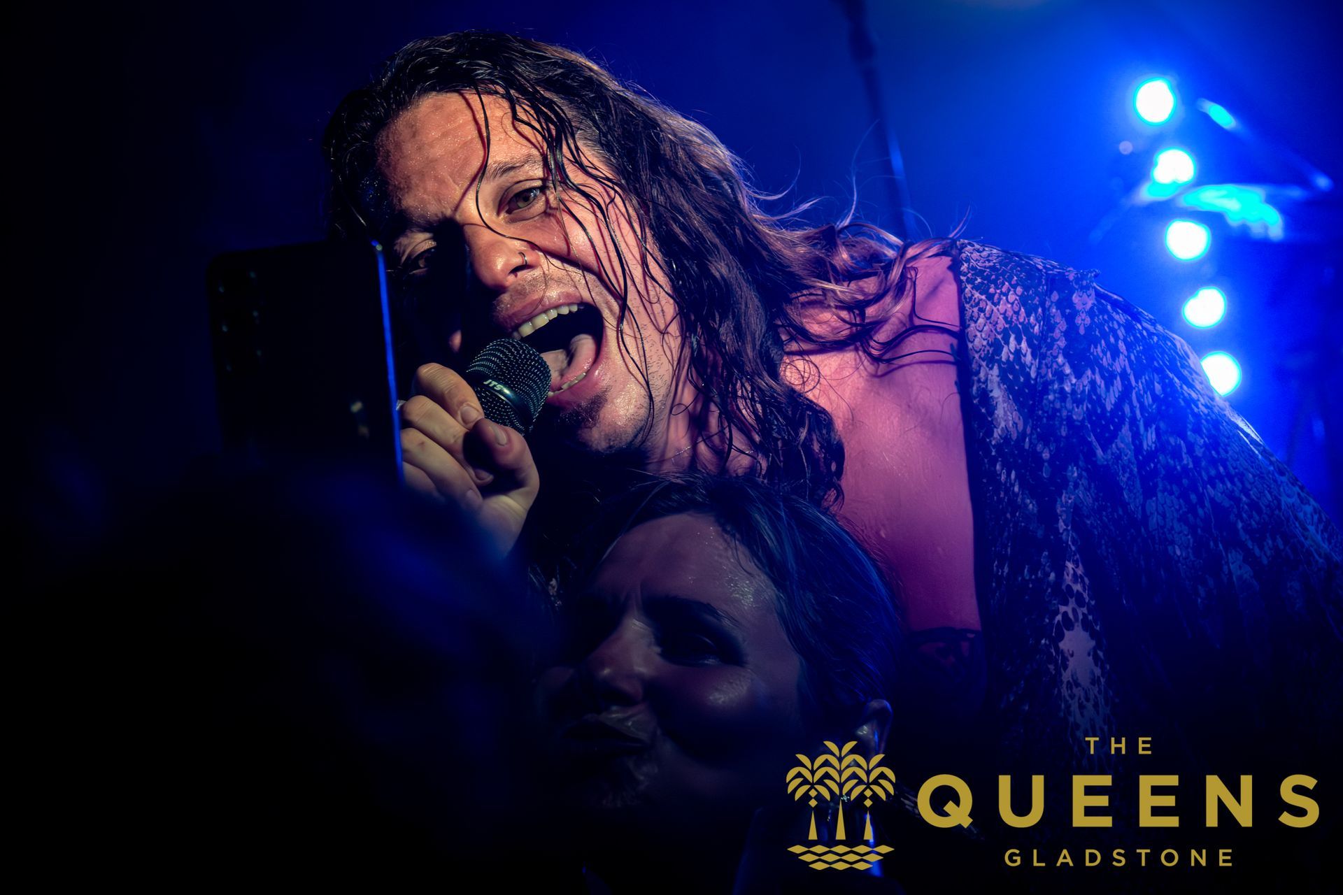 Singer performing on stage under blue lights, holding a microphone, with
