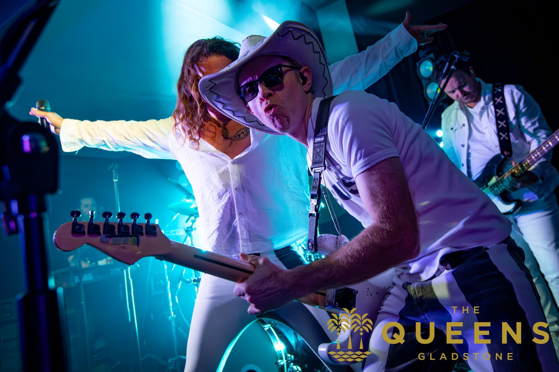 Country band performing onstage under blue lights, with a guitarist in a cowboy hat in the foreground.
