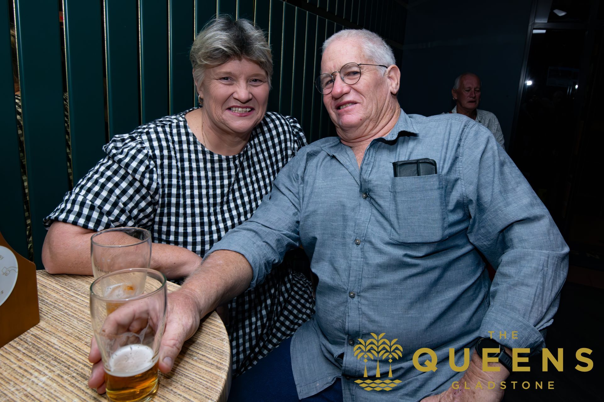 Two people smiling at a table, holding drinks in a dimly lit lounge.